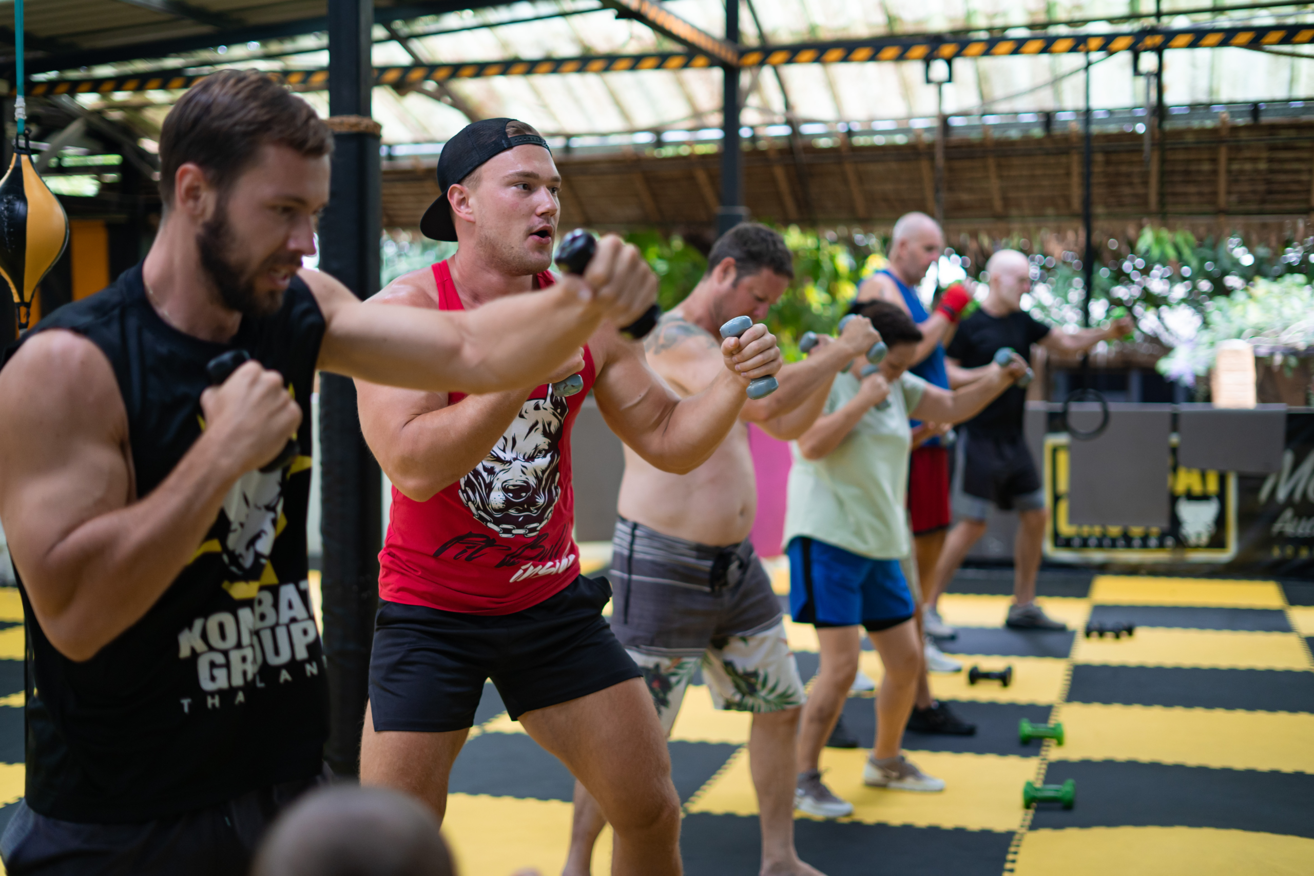 A diverse group of individuals practicing boxing punches in a gym with a focus on technique and form, as they train on a yellow and black matted floor.